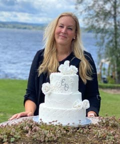 Bild på Anna Grund bakom en vit bröllopstårta.